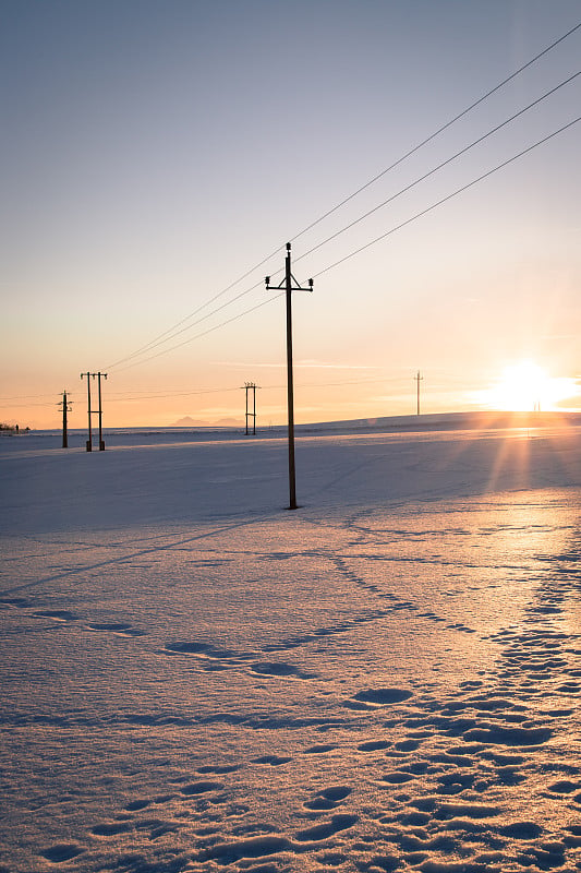 雪地上的电力塔。夕阳西下，橘色的夜景