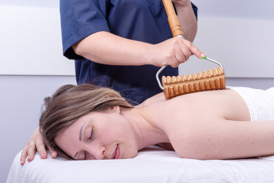 女士在美容院用木制滚轮按摩器做spa背部按摩。身体护理的概念