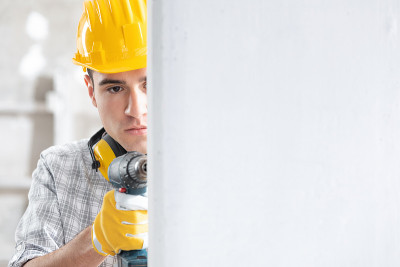年轻男性建筑工人在墙上钻孔