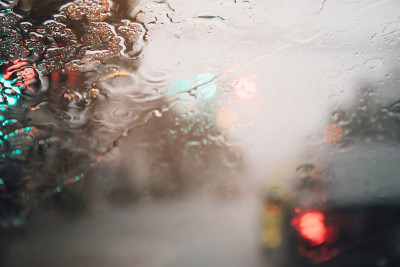 傍晚，细雨落在挡风玻璃上。街道在大雨中。散景尾灯。软的焦点。路滑，请小心驾驶。软的焦点。