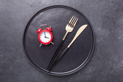Red alarm clock, fork, knife and empty black ceram