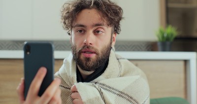 一名男子在家与医生视频通话，被发现流鼻涕。用智能手机与全科医生进行视频会议。