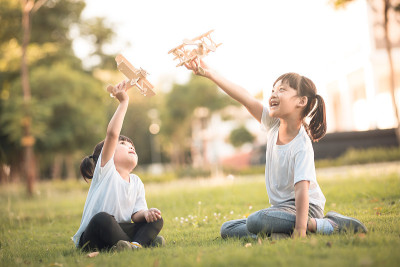 两个小孩白天在公园里玩纸板做的玩具飞机。快乐游戏的概念。孩子在户外玩耍。