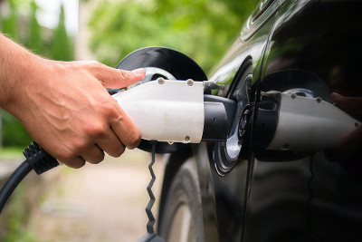 在绿色环境背景下，人工将充电器插入电动汽车。新能源汽车、新能源汽车正在装载电力。生态，现代汽车