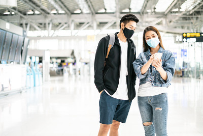 新常态、泡沫旅行和社交距离概念。在病毒大流行期间，一名男子和一名女子戴着口罩，在候机楼等待登机，以保