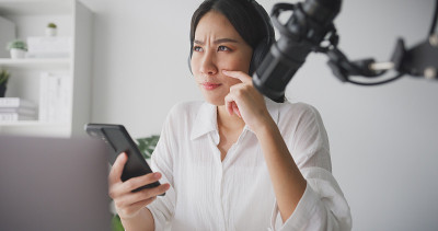 一名年轻的亚洲女性在家庭录音室用笔记本电脑录制播客。