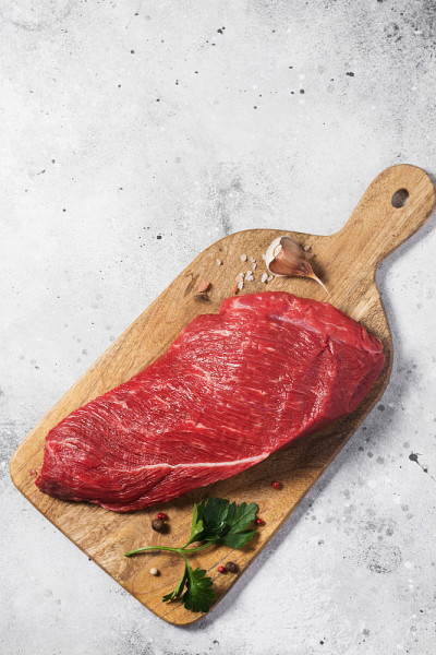 灰色餐桌上的一块木板上放着生牛肉。顶部视图与复制空间