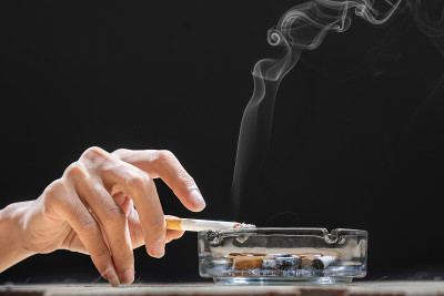 手拿一根香烟，放在有透明烟灰缸的木桌上
