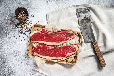 木托盘上的生西冷牛排和切肉刀。大理石牛肉。灰色的背景。俯视图