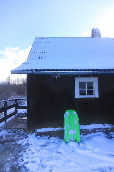 绿色的塑料雪橇在乡村房屋墙边的雪地上滑行