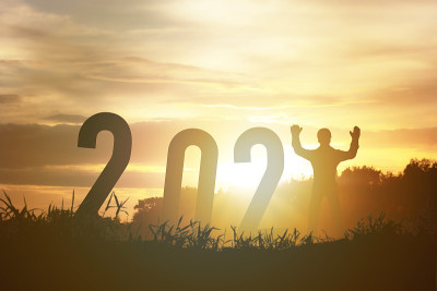 2021年新年快乐剪影概念人站在数字和美丽的橙色天空变化到2021年。
