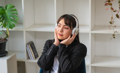 年轻的亚洲女性戴着耳机在办公室享受着音乐放松工作。
