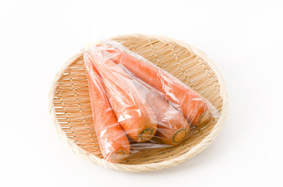 新鲜胡萝卜装于塑料袋，竹制滤锅，白色背景