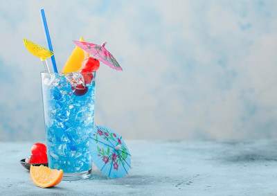蓝色泻湖夏季鸡尾酒在高球杯甜鸡尾酒樱桃和橙色切片与伞在蓝色背景。