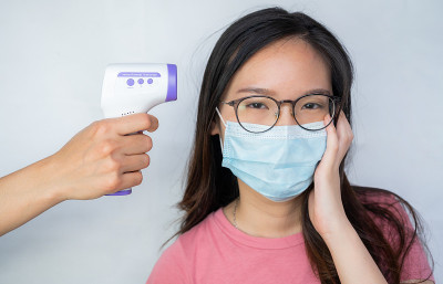 有人手持红外测温枪测量亚洲女性体温。