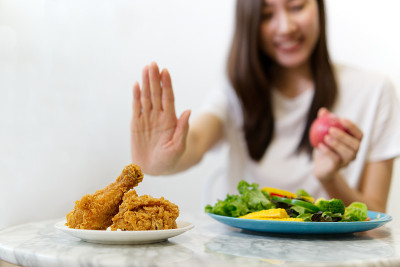 年轻女孩节食为良好的健康观念。近距离女性用手拒绝垃圾食品推出她最喜欢的炸鸡和选择红苹果和沙拉为健康。