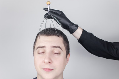 一个男人在沙龙里用毛细管按摩器做头部按摩。客户的脸上流露出放松和喜悦。抗压力按摩的概念和由按摩师提供