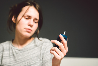 主题糖尿病。年轻的白种妇女在家中卧室的床上使用技术设备来测量血糖，血糖仪检测出高血糖水平的疾病