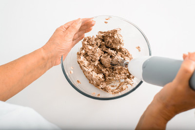 俯视图妇女的手准备奶油馅饼馅，家庭主妇搅拌原料使用搅拌机搅拌机在室内桌上。退休妇女的爱好是在家里的厨