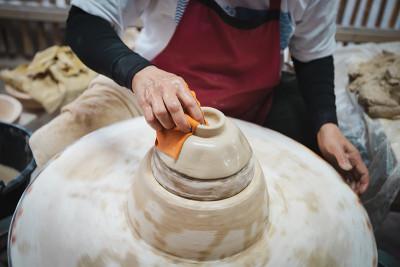 陶工大师在陶工轮上用白色粘土制作陶瓷产品。手用陶罐雕刻一个碗。