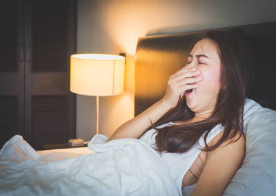 年轻美丽的亚洲女人打呵欠和感觉困在卧室的白色床上。