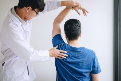 理疗医生在理疗室协助男性病人进行运动治疗，并按摩病人的肩膀，这是康复理疗的概念