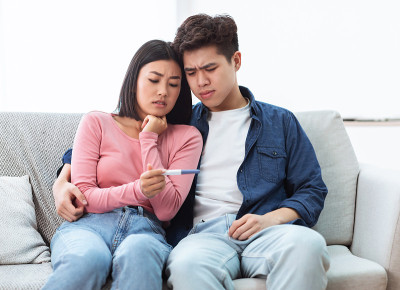 沮丧的亚洲夫妇拿着阴性怀孕测试坐在家里