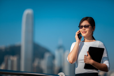 一位商务女性正拿着笔记本打电话，走在香港海滨