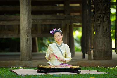 亚洲女士与微笑在泰国传统想要打扮坐和演奏扬琴