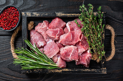 生切碎的猪肉幼崽肉与香料在一个质朴的托盘。黑色木制背景。俯视图