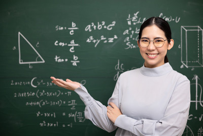 年轻的亚洲女教师张开手，手掌向上，与学生看着摄像机进行视频会议。女教师从网络课程培训数学课堂黑板。