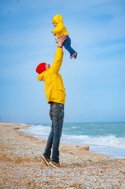 爸爸穿着五颜六色的衣服和一个婴儿在海边。