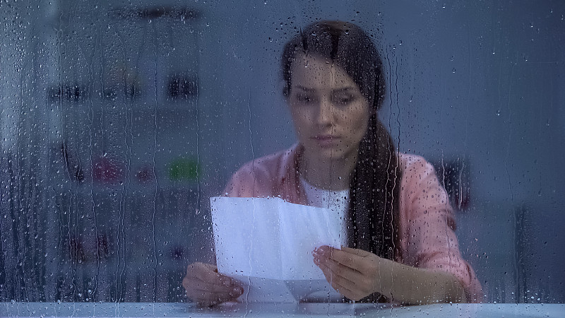 沮丧的女性躲在雨窗后读信，亲戚传来坏消息