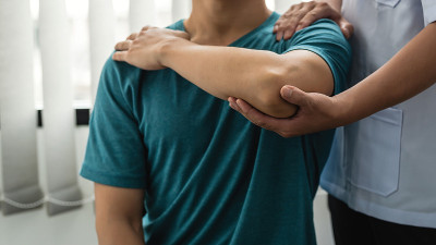 男理疗师在诊所协助肘部受伤的男病人。