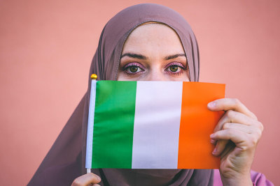 Muslim woman in a scarf holds flag of Ireland