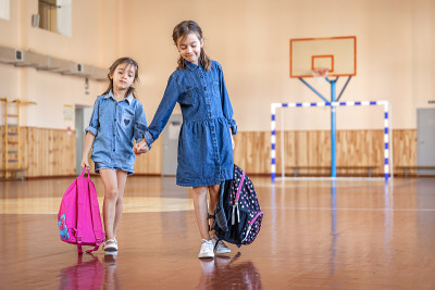 空空的学校体育馆里背着书包的小女孩们。