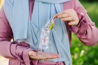 这个女孩拿着一个罐子准备睡觉。Hijama，放血，治疗sunna。在树木和绿色植物的背景下放血用的罐