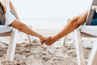 一对情侣坐在沙滩椅上，手牵着手在早上的海滩上。一对新婚夫妇在浪漫的假期