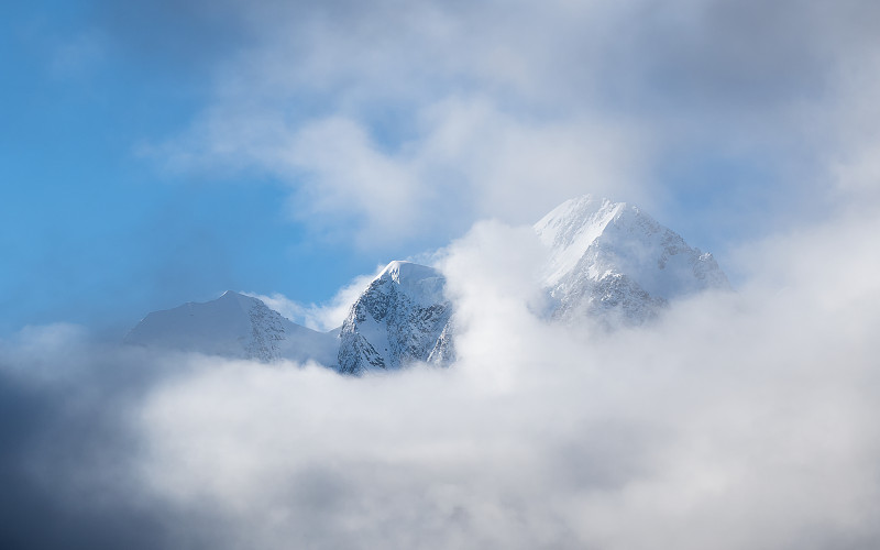 全景高山阳光景观高雪山与尖顶和冰川之上的低云。大雪山被阳光覆盖。阳光下的白雪尖峰。