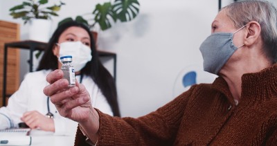 混血药房女医生在门诊检查时将装有疫苗药物的烧瓶给资深白种病人女。