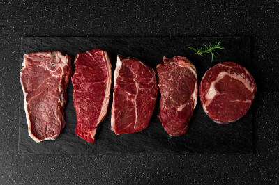 选择生牛肉肉排，以黑石为背景。纽约striploin牛排，顶级刀片，肋眼，和其他切肉。