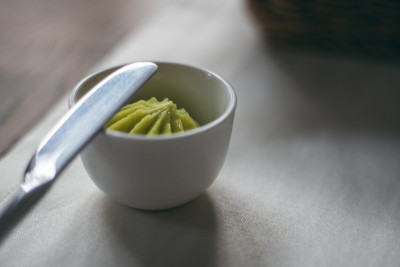 木桌上的白桌布上放着一碗自制的绿色黄油、香草和小刀