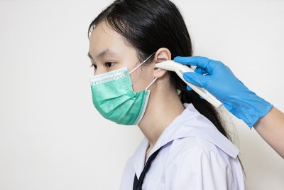 亚洲少女穿着校服在耳道测量体温，医生用数字耳温计检查发烧，学生健康检查，医学检查概念