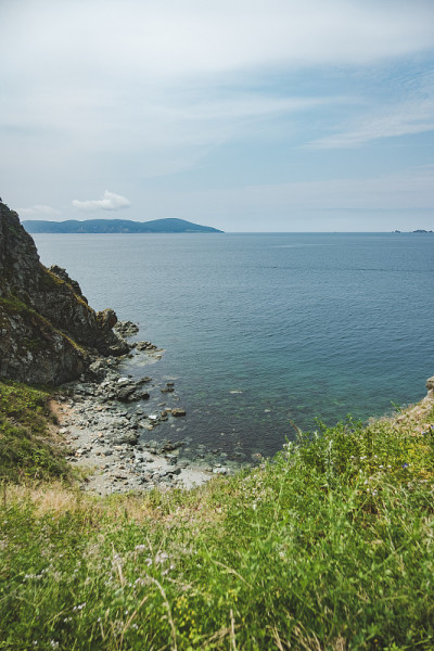 夏日蔚蓝清澈的大海全景。浅浅的透明的海洋，周围有珊瑚礁、岩石和绿色的小山。日本海洋。俄罗斯的滨海边疆