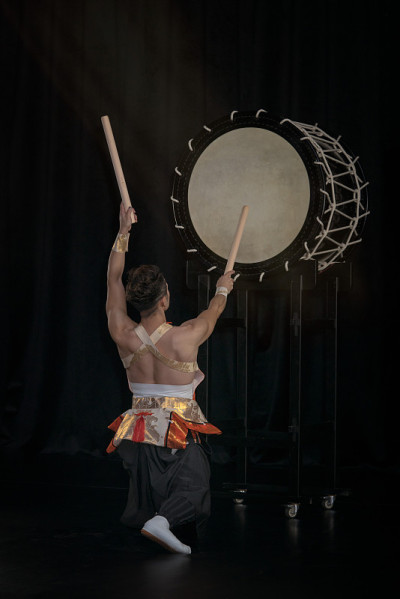 Taiko鼓手在舞台上敲着大鼓，背景为黑色，背景为背景。