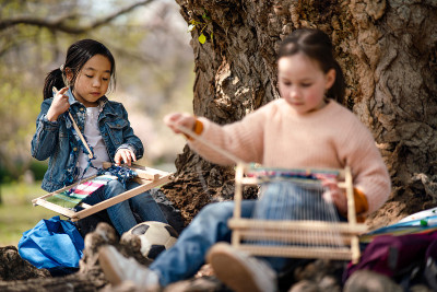 幼儿用手织布机坐在户外城市公园，学习小组教育理念。