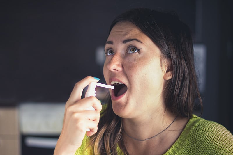 女孩喉咙痛，用喷雾剂喷了一口。治疗感冒流感