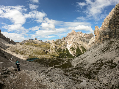 一名女子背着背包，拄着拐杖在意大利Dolomites的一条狭窄小路上徒步旅行。那里有陡峭的山。在一个