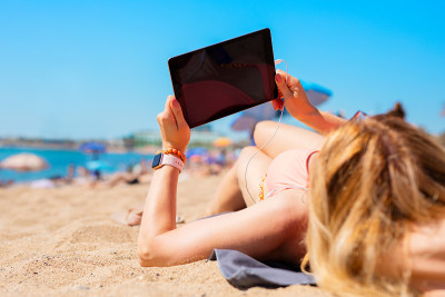在炎热的夏天，在海滩上用平板电脑的女人