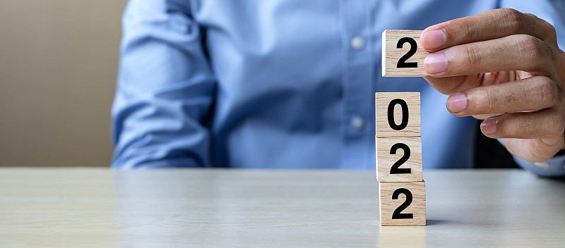 商人手握木制方块与2022文本的桌子背景。决心，策略，解决方案，目标，业务，新年新你和快乐假期的概念